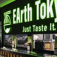 Restaurant mit grünem Leuchtschild 'EArth Tokyo' und dem Slogan 'Just Taste It'. Moderne Einrichtung mit Pflanzenwand., © SMG, Sarah Schmid Restaurant mit grünem Leuchtschild 'EArth Tokyo' und dem Slogan 'Just Taste It'. Moderne Einrichtung mit Pflanzenwand., © SMG, Sarah Schmid