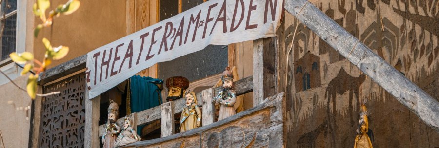 A wooden balcony with puppets and a hand-painted banner 'Theater am Faden'. The puppets are traditionally dressed., &copy; SMG Stuttgart Marketing GmbH - Sarah Schmid