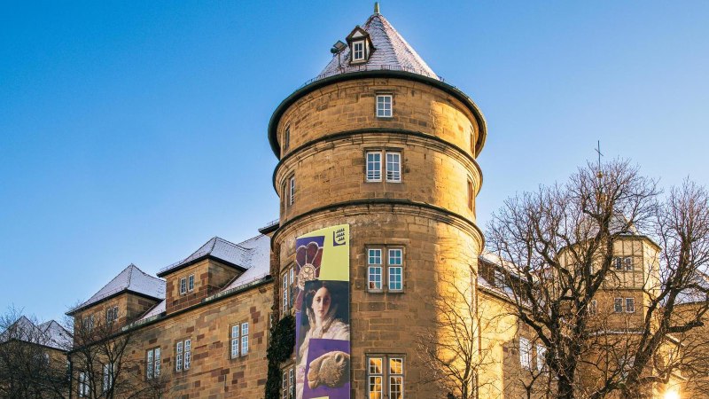 Das Alte Schloss in Stuttgart bei klarem Himmel. Ein Werbebanner schm&uuml;ckt die Fassade. Die Sonne scheint durch die kahlen B&auml;ume., &copy; Stuttgart-Marketing GmbH, Sarah Schmid