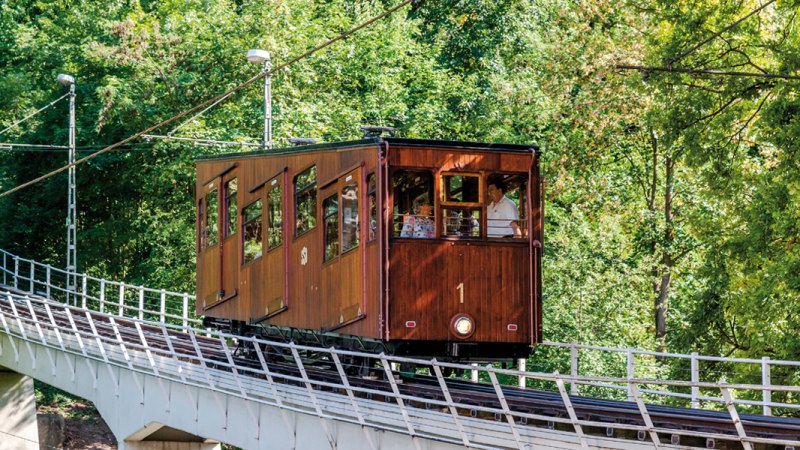 A historic funicular with wooden cladding runs along an inclined track surrounded by dense greenery., © TMBW, Gregor Lengler