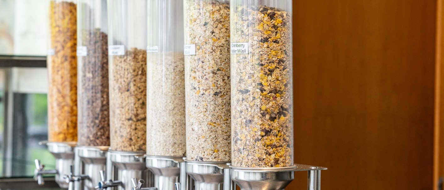 Mehrere transparente Spender mit verschiedenen Müslisorten in einem Frühstücksbuffet, bereit zur Selbstbedienung., © PLAZA INN Rieker Stuttgart Hauptbahnhof Mehrere transparente Spender mit verschiedenen Müslisorten in einem Frühstücksbuffet, bereit zur Selbstbedienung., © PLAZA INN Rieker Stuttgart Hauptbahnhof