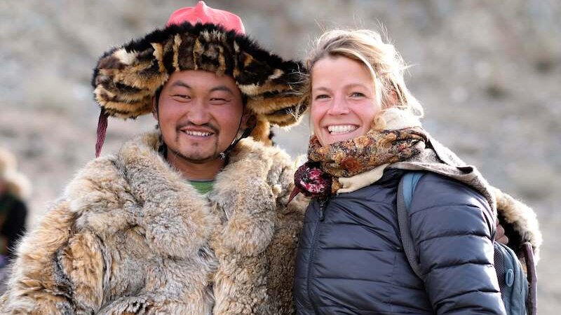 A man in traditional fur clothing and a woman in modern winter clothing smile at the camera. They are standing in front of a blurred background outdoors., © Theaterhaus Stuttgart e.V. A man in traditional fur clothing and a woman in modern winter clothing smile at the camera. They are standing in front of a blurred background outdoors., © Theaterhaus Stuttgart e.V.