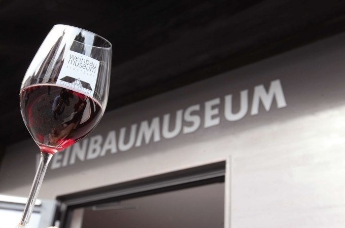 Ein Weinglas mit Rotwein wird vor dem Eingang des Weinbaumuseums in die Höhe gehalten., © Stuttgart Marketing GmbH, Thomas NIedermüller