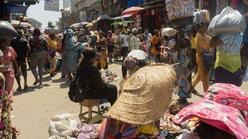 Belebter Markt in Lagos mit zahlreichen Menschen, die Waren kaufen und verkaufen. Farbenfrohe Kleidung und gesch&auml;ftiges Treiben pr&auml;gen das Bild., &copy; Dandara Maia