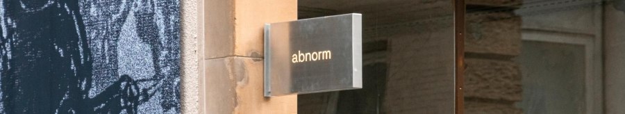 A metal sign with the words 'abnormal' hangs on a wall. Next to it is an art poster., © SMG, Sarah Schmid A metal sign with the words 'abnormal' hangs on a wall. Next to it is an art poster., © SMG, Sarah Schmid
