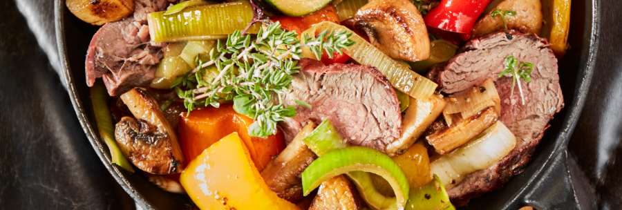Pan with roasted meat, zucchini, peppers, mushrooms and herbs, served on a wooden board., © MAREDO