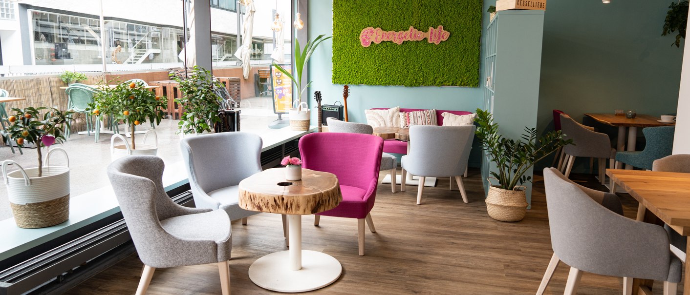 Bright café with modern gray and pink chairs, wooden tables and green plants. Large window front and green moss wall with "Energetic life" lettering., © � 2022 Anastasiia Vovk, all rights reserved. Bright café with modern gray and pink chairs, wooden tables and green plants. Large window front and green moss wall with "Energetic life" lettering., © � 2022 Anastasiia Vovk, all rights reserved.