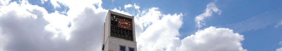 A modern building with a tall clock tower and lots of windows. The sky is blue with a few clouds., © Fei Shiyu