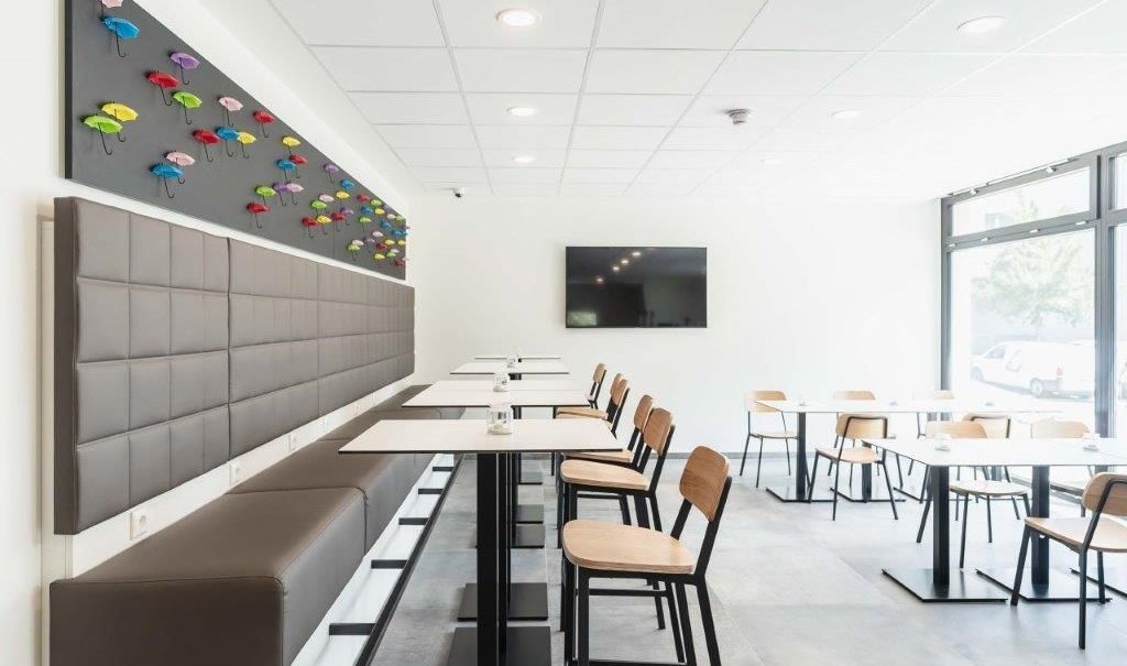 A modern breakfast area with white tables, wooden chairs, and colorful umbrella decorations on the wall., &copy; a2 HOTELS am Quadrium