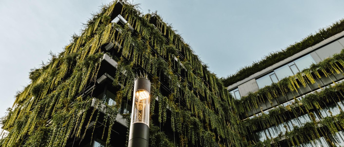 Ein modernes Geb&auml;ude mit einer gr&uuml;nen Fassade, bedeckt von h&auml;ngenden Pflanzen. Im Vordergrund steht eine beleuchtete Stra&szlig;enlaterne., &copy; Stuttgart-Marketing GmbH, Sarah Schmid