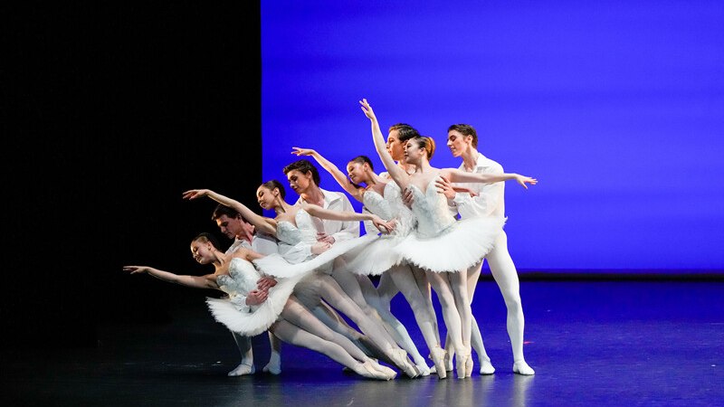 Ballet dancers in white costumes pose synchronously on a stage in front of a blue background. Elegant and harmonious choreography., &copy; W&uuml;rttembergische Staatstheater Stuttgart