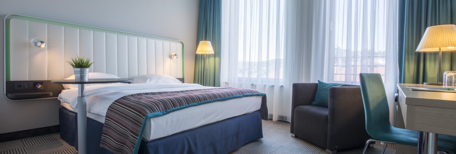 Modern hotel room with double bed, desk, armchair and large windows. The furnishings are in shades of blue and white., © Park Inn by Radisson Stuttgart Modern hotel room with double bed, desk, armchair and large windows. The furnishings are in shades of blue and white., © Park Inn by Radisson Stuttgart