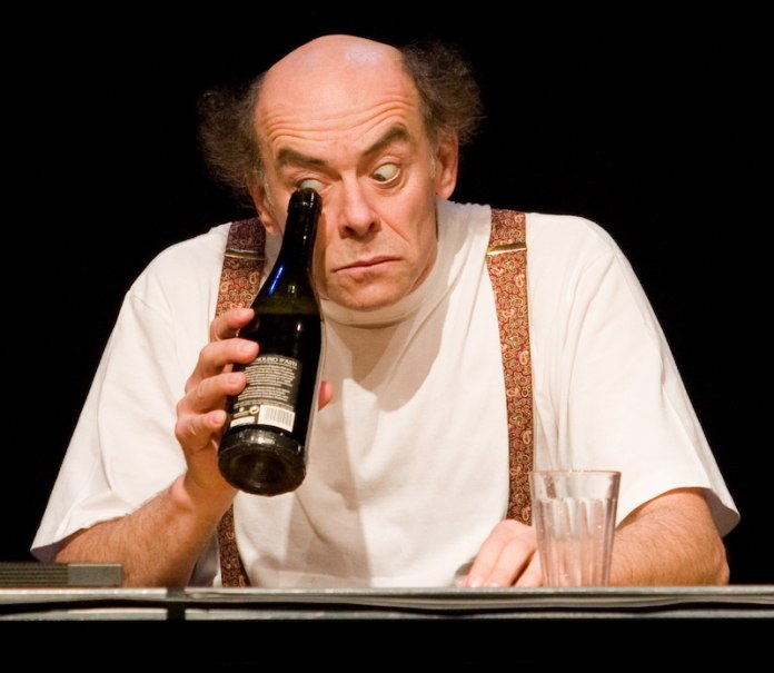 Ein Mann mit Glatze und Hosenträgern schaut durch eine Flasche. Vor ihm steht ein Glas auf dem Tisch., © Theaterhaus Stuttgart e.V. Ein Mann mit Glatze und Hosenträgern schaut durch eine Flasche. Vor ihm steht ein Glas auf dem Tisch., © Theaterhaus Stuttgart e.V.