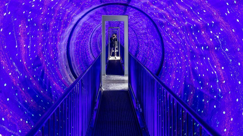Ein beleuchteter Tunnel mit blauen und violetten Lichtern im Museum der Illusionen Stuttgart. Eine Person steht am Ende des Tunnels., &copy; Stuttgart-Marketing GmbH, Sarah Schmid