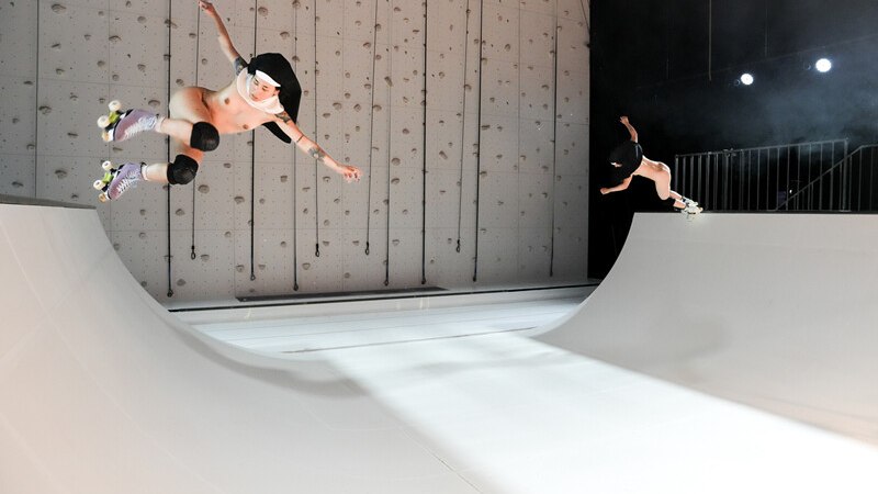 Zwei Personen in Rollschuhen führen Tricks auf einer weißen Halfpipe aus. Sie tragen Helme und Knieschützer. Der Hintergrund ist eine Kletterwand., © Württembergische Staatstheater Stuttgart Zwei Personen in Rollschuhen führen Tricks auf einer weißen Halfpipe aus. Sie tragen Helme und Knieschützer. Der Hintergrund ist eine Kletterwand., © Württembergische Staatstheater Stuttgart