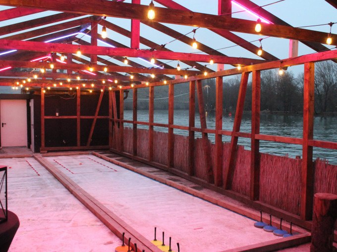 Covered curling rink with colorful fairy lights, view of a river in the background. The rink is made of wood and equipped with curling sticks., &copy; Cool-Tours StattReisen