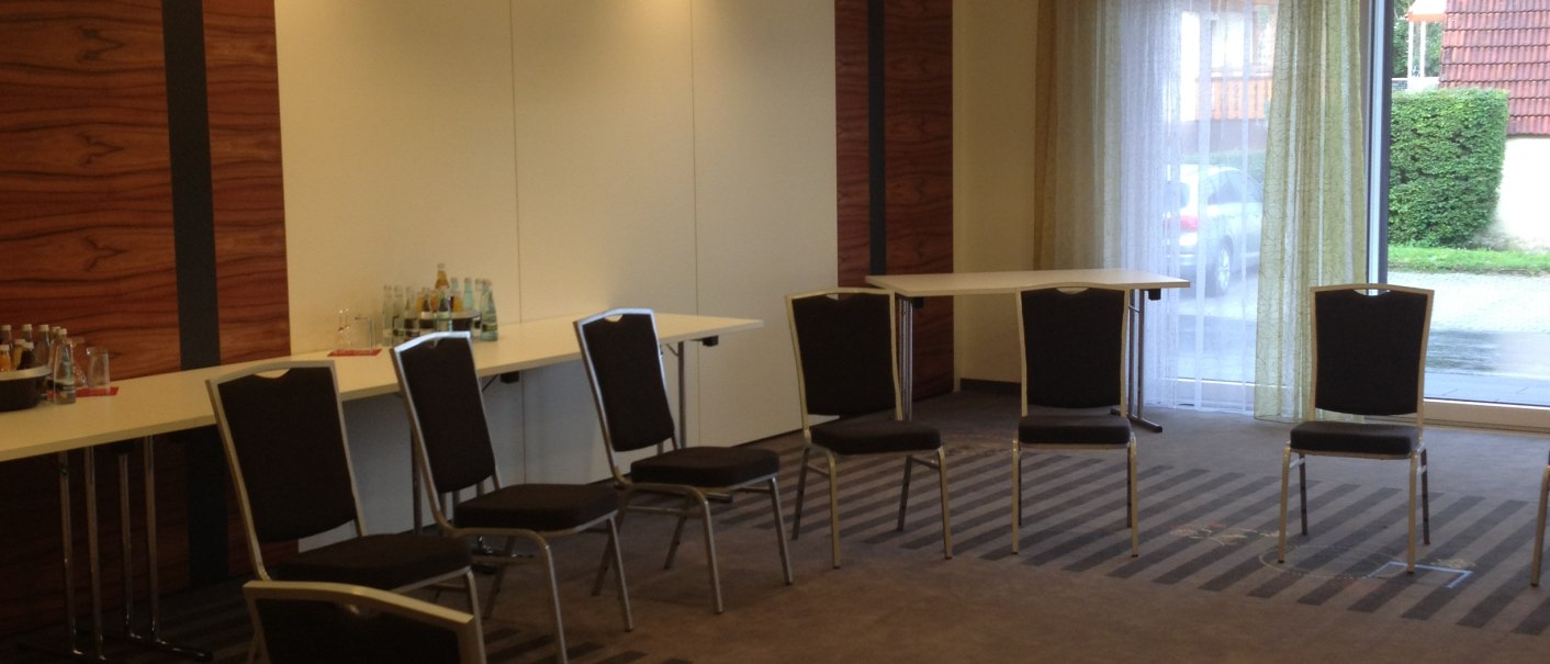 An empty meeting room with chairs in a circle and tables against the wall. The lighting is warm and a chandelier hangs from the ceiling., © Hotel & Restaurant Sonne