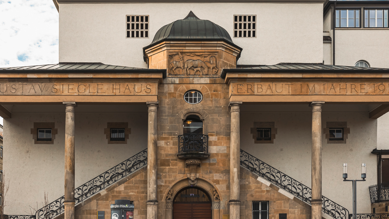 Das Gustav-Siegle-Haus zeigt eine Fassade mit Säulen und der Inschrift 'GUSTAV SIEGLE HAUS ERBAUT IM JAHRE 1912'. Es hat ein klassisches Design., © Stuttgart-Marketing GmbH, Sarah Schmid Das Gustav-Siegle-Haus zeigt eine Fassade mit Säulen und der Inschrift 'GUSTAV SIEGLE HAUS ERBAUT IM JAHRE 1912'. Es hat ein klassisches Design., © Stuttgart-Marketing GmbH, Sarah Schmid