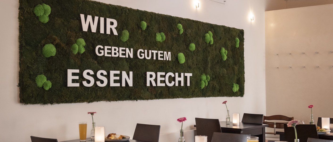 Restaurant with a moss wall and the slogan 'We do right by good food'. Dark tables, candles and flowers decorate the room., © Andreas Dalferth