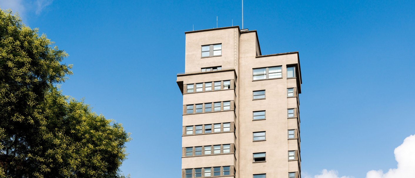 Der Tagblatt-Turm in Stuttgart erhebt sich vor einem klaren blauen Himmel, umgeben von gr&uuml;nen B&auml;umen., &copy; TMBW, Gregor Lengler