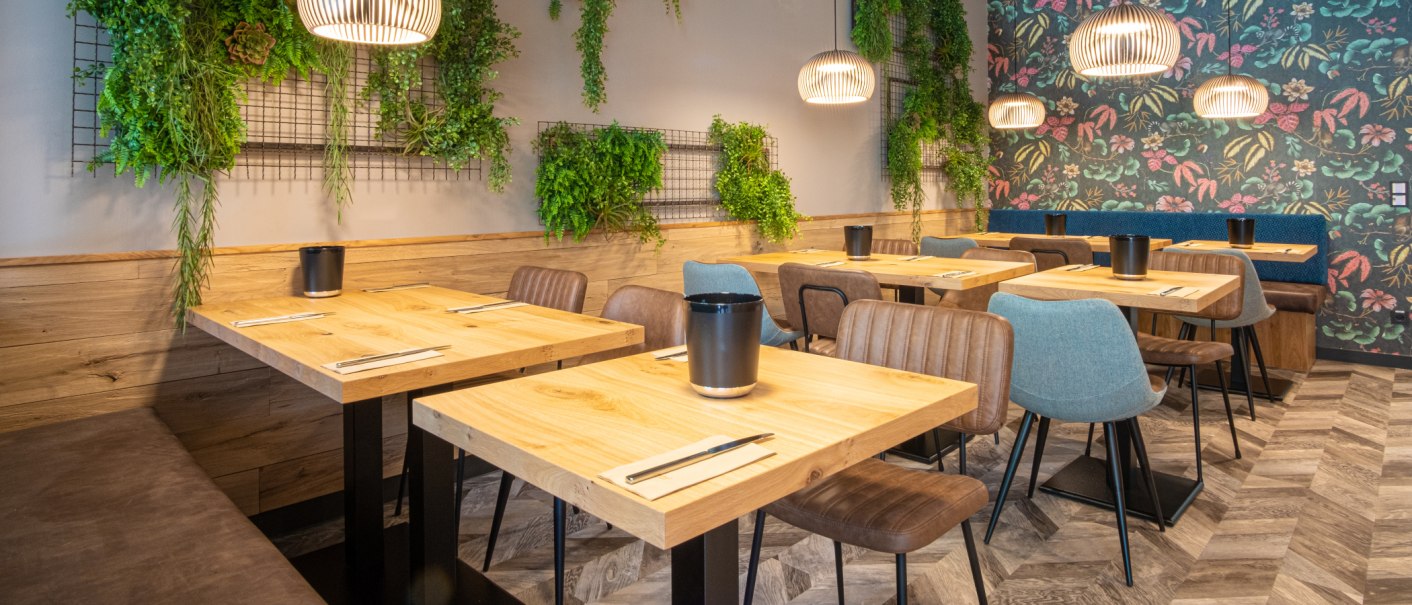 Moderner Fr&uuml;hst&uuml;cksraum mit Holztischen, bunten St&uuml;hlen und Pflanzen an der Wand. H&auml;ngelampen und florale Tapete erg&auml;nzen das Design., &copy; 13 6 Design GmbH (Judenhof 10, 89073 Ulm)