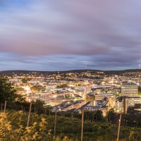 Panorama einer Stadt bei Abenddämmerung, mit beleuchteten Gebäuden und einem bewölkten Himmel im Hintergrund., © SMG, Werner Dieterich Panorama einer Stadt bei Abenddämmerung, mit beleuchteten Gebäuden und einem bewölkten Himmel im Hintergrund., © SMG, Werner Dieterich