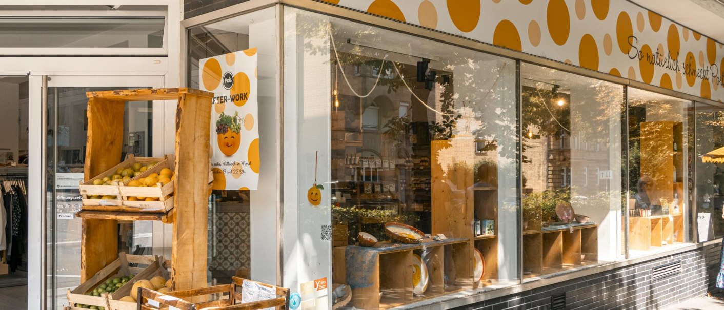 Geschäft 'Pois' mit gelb-orange gepunktetem Schild, Obstkisten vor dem Eingang, große Fensterfront., © SMG; Sarah Schmid