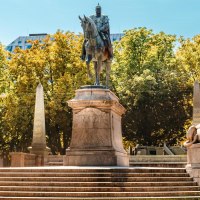 Reiterstatue auf dem Karlsplatz, flankiert von zwei Löwenstatuen. Umgeben von Bäumen und modernen Gebäuden im Hintergrund., © Stuttgart Marketing GmbH, Sarah Schmid Reiterstatue auf dem Karlsplatz, flankiert von zwei Löwenstatuen. Umgeben von Bäumen und modernen Gebäuden im Hintergrund., © Stuttgart Marketing GmbH, Sarah Schmid