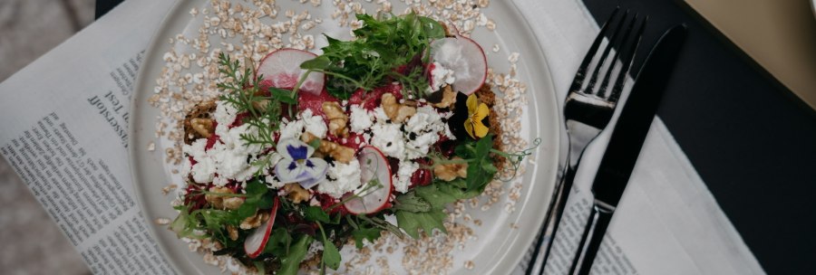 A decorative salad with radishes, nuts and edible flowers on a plate, served on a newspaper., © Fritz, Stuttgart
