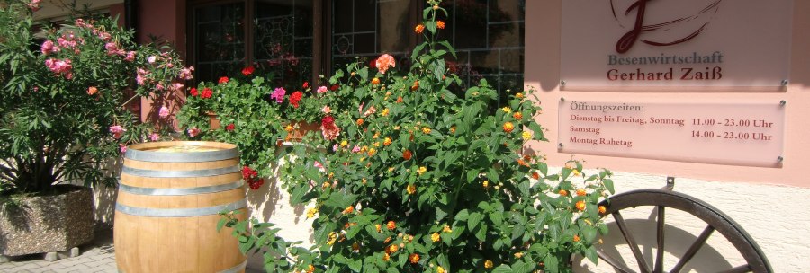 Entrance to the Besenwirtschaft Gerhard Zai&szlig; with flowering plants, a wine barrel and a sign with opening hours., &copy; Simone Mack