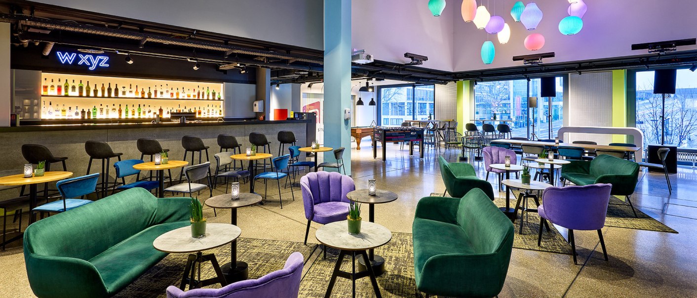 Modern lounge with colorful armchairs and sofas, stylish bar and colorful lamps. Large windows offer a view to the outside., &copy; aloft Stuttgart