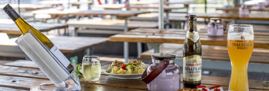 Beer garden with wooden tables, white wine, Malteser wheat beer, white sausages, pretzels and potato salad. A river can be seen in the background., © all copyrights are reserved by maks richter