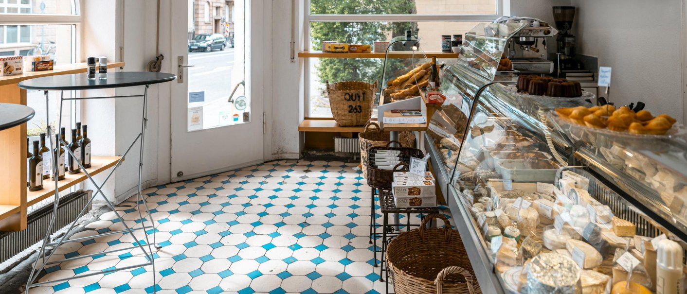 A delicatessen with cheese display, pastries and bottles of wine. Light-colored tiles and a window with a view of the street., © SMG, Sarah Schmid A delicatessen with cheese display, pastries and bottles of wine. Light-colored tiles and a window with a view of the street., © SMG, Sarah Schmid