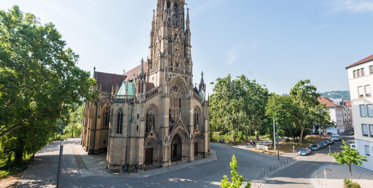 Blick auf die Kirche am Feuersee in Stuttgart, umgeben von B&auml;umen und Stra&szlig;en bei klarem Himmel., &copy; ARNOTEL GmbH