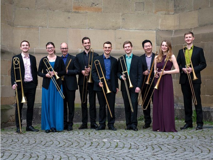 Neun Personen in festlicher Kleidung halten Posaunen und stehen vor einer Steinwand. Sie l&auml;cheln und posieren f&uuml;r ein Gruppenfoto., &copy; Landesmuseum W&uuml;rttemberg