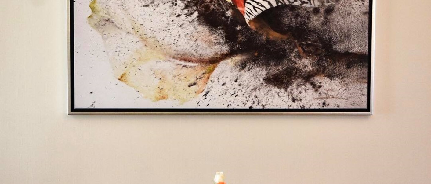 A breakfast table with four place settings, a black table runner and a vase with a flower. An abstract work of art hangs on the wall., &copy; TOMAS