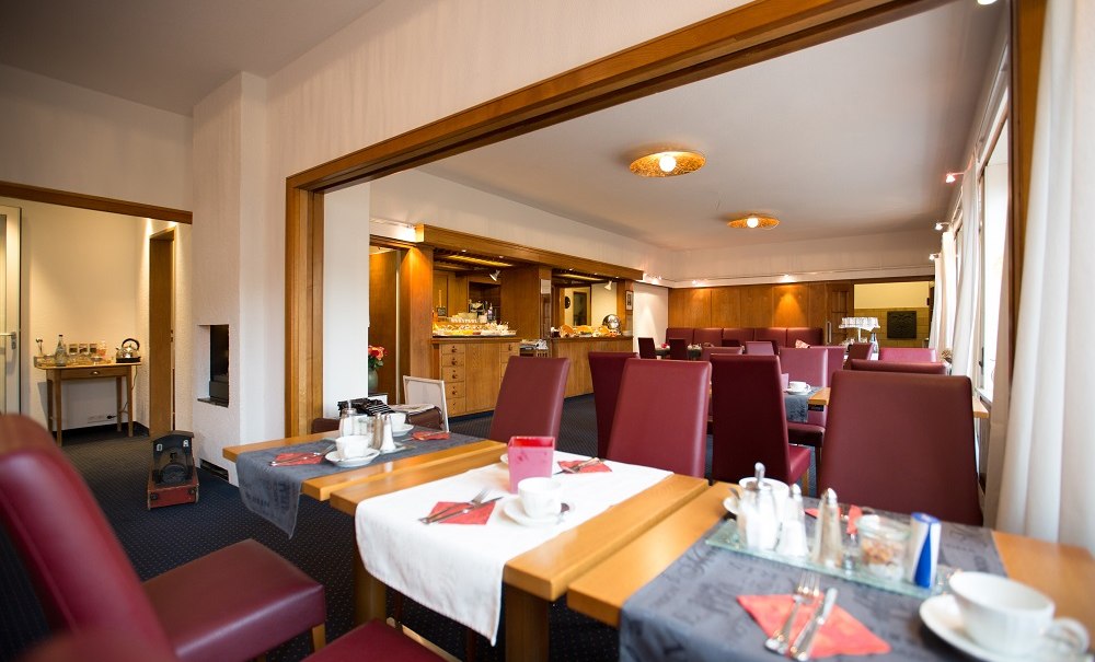 A breakfast room with red chairs, set tables, and a buffet in the background. Warm lighting and wooden accents create a welcoming atmosphere., &copy; Hotel B&uuml;rkle