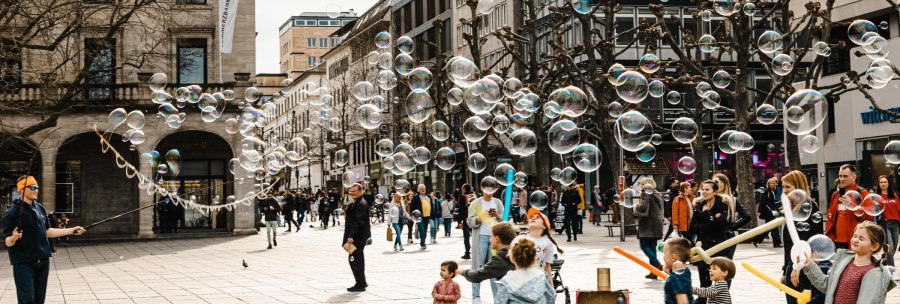 A street artist creates soap bubbles on a busy street. Children play enthusiastically with the bubbles while passers-by look on., &copy; Stuttgart-Marketing GmbH, Sarah Schmid