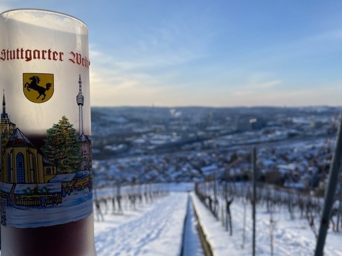 Ein Glas Glühwein mit Stuttgarter Motiv steht vor einer verschneiten Weinberglandschaft. Im Hintergrund ist die Stadt Stuttgart zu sehen., © Weingenuss Stuttgart Ein Glas Glühwein mit Stuttgarter Motiv steht vor einer verschneiten Weinberglandschaft. Im Hintergrund ist die Stadt Stuttgart zu sehen., © Weingenuss Stuttgart