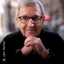 A man with glasses and gray hair smiles friendly into the camera. He is wearing a black sweater and has his hands folded under his chin., &copy; links im Bild