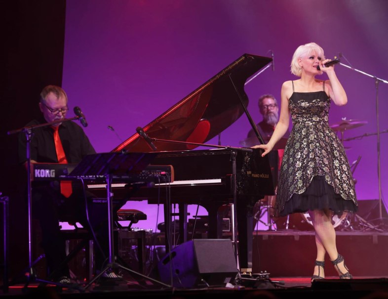 Eine Frau singt auf einer Bühne neben einem Klavierspieler. Der Hintergrund ist in lila Licht getaucht., © Friedrichsbau Varieté Eine Frau singt auf einer Bühne neben einem Klavierspieler. Der Hintergrund ist in lila Licht getaucht., © Friedrichsbau Varieté