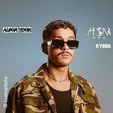 Ein Mann in Tarnjacke und Sonnenbrille steht vor einem blauen Hintergrund. Text: "Album Tour", "HOW", "KYBBA"., © links im Bild Ein Mann in Tarnjacke und Sonnenbrille steht vor einem blauen Hintergrund. Text: "Album Tour", "HOW", "KYBBA"., © links im Bild