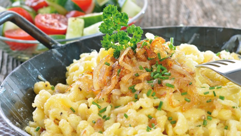 Cheese spaetzle with fried onions and chives in a pan, served with a fresh salad of tomatoes and cucumber., © kab-vision - Fotolia