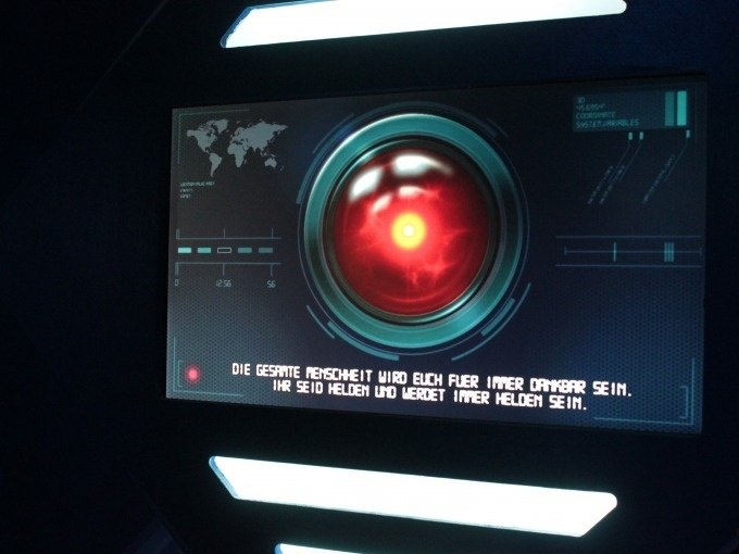 Screen with red eye and text message about heroism. World map and technical displays in the background., © ExitGames Stuttgart Screen with red eye and text message about heroism. World map and technical displays in the background., © ExitGames Stuttgart
