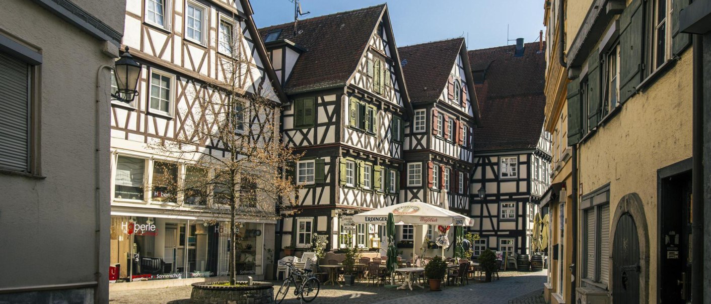 Half-timbered houses on Schorndorf's market square. A caf&eacute; with umbrellas and tables is in the foreground. The scene has a welcoming and historic feel., &copy; SMG Stuttgart Marketing GmbH - Sarah Schmid