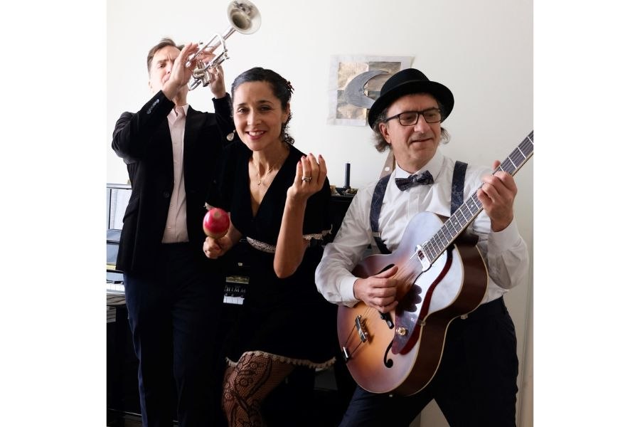 A trio of musicians in a room: a trumpet player, a woman with a maraca and a guitarist with a hat. They appear concentrated and passionate., &copy; PaperMoon