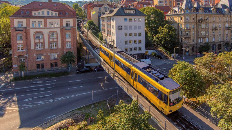 The cog railroad in Stuttgart runs on an elevated track through an urban environment with historic buildings and trees., © SMG, Achim Mende