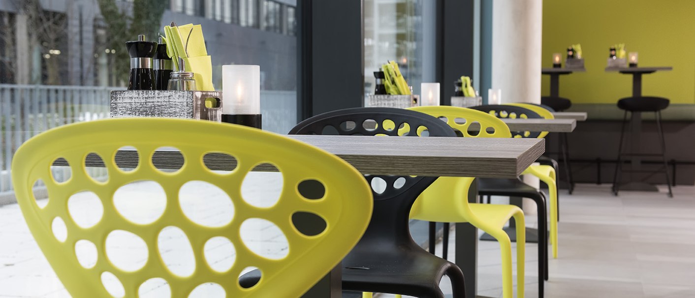 Modernes Restaurant mit gelben und schwarzen Stühlen, gedeckten Tischen und großen Fenstern., © ibis Styles Stuttgart Vaihingen
