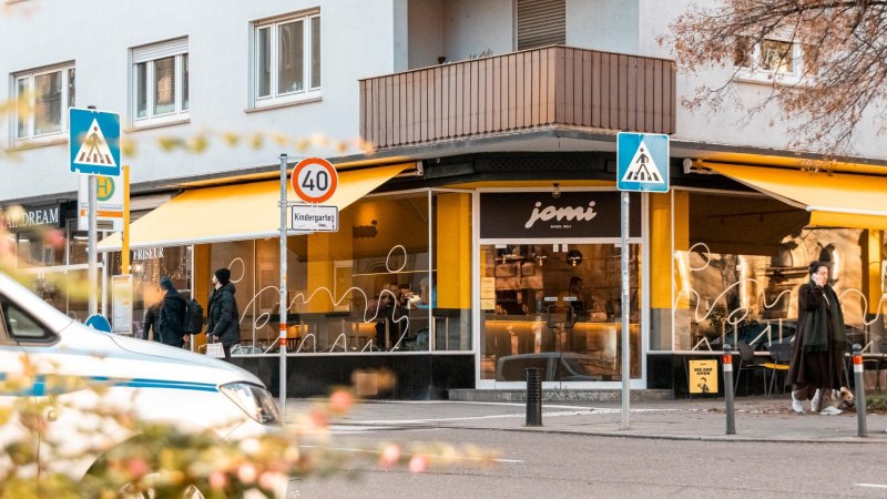 Schaufenster des Deli mit gelben Markisen. &Uuml;ber der T&uuml;r am Eck des Geb&auml;udes steht "jomi Bagel Deli"., &copy; Stuttgart-Marketing GmbH, Sarah Schmid
