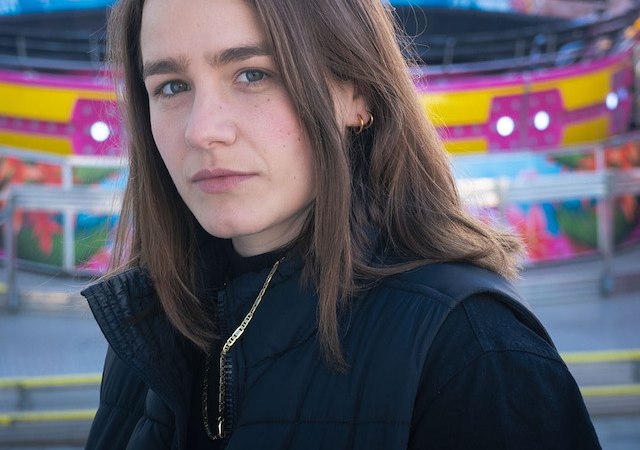 Woman with brown hair and black vest stands in front of a colorful, blurred background with bright colors and patterns., &copy; Renitenztheater Stuttgart e.V.